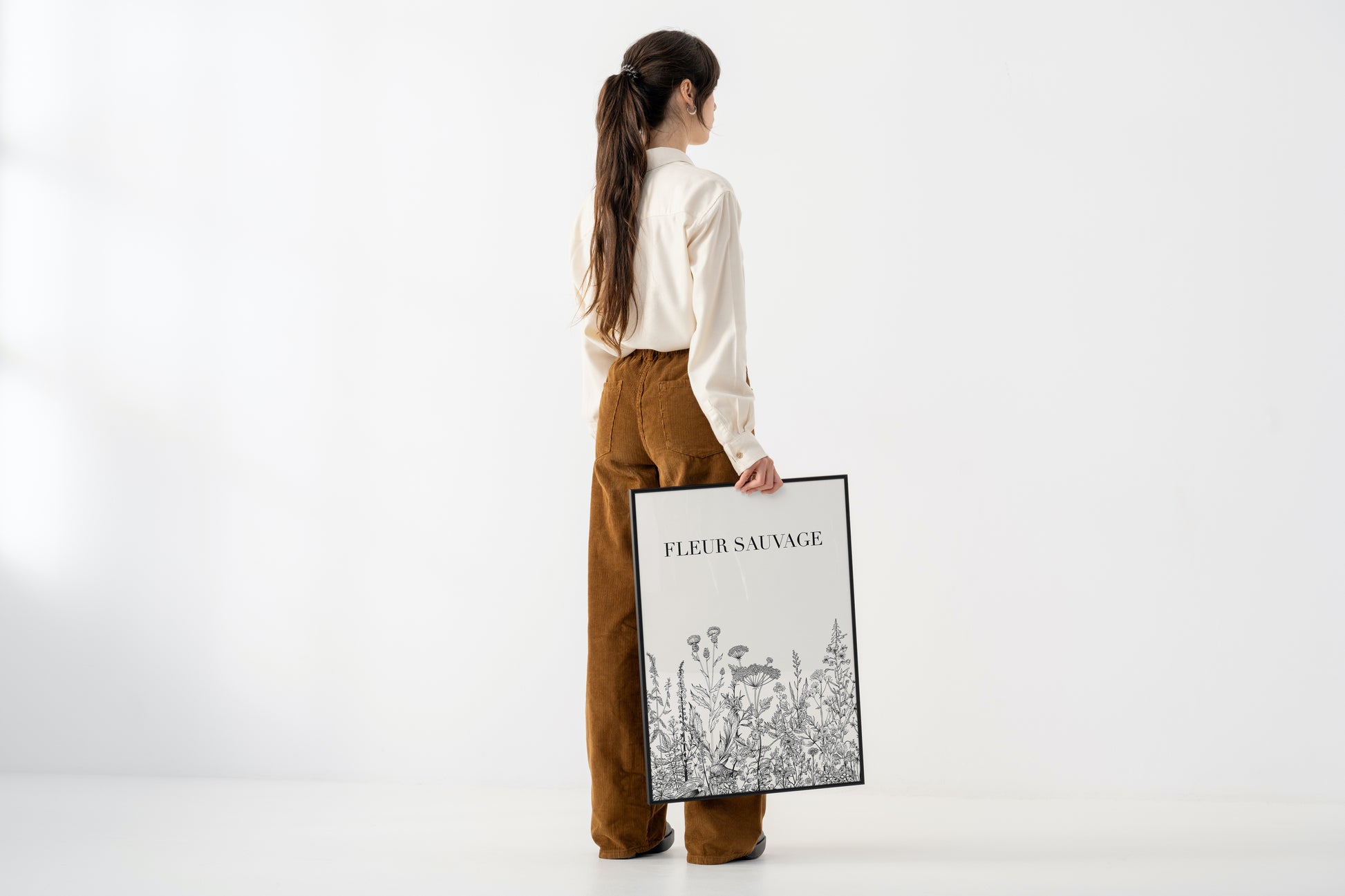 Woman holding a framed artwork titled 'Fleur Sauvage' on a white background